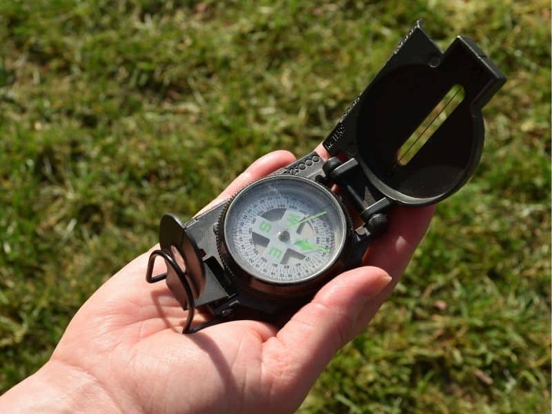 Hand hält einen geöffneten Kompass im Grünen